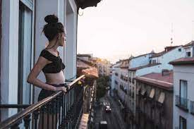 Beautiful young woman on balcony above the city at sunset stock photo